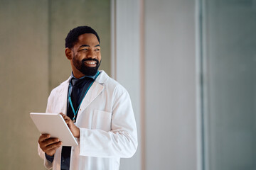 Happy black doctor using touchpad while working at medical clinic.