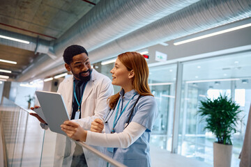 Happy healthcare workers using wireless technology while talking in hospital.
