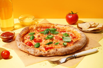 Baking paper with tasty pizza Margarita and plate of potato chips on yellow background