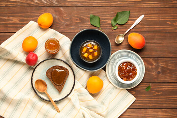 Bowls with sweet apricot jam and toast on wooden background