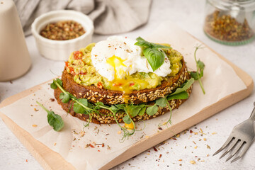 Wooden board of tasty sandwich with egg on light background