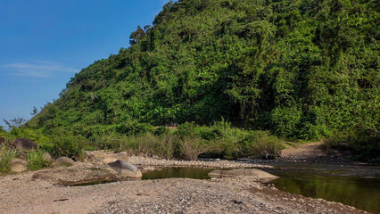 Rocky riverbank with lush green hillside, serene nature landscape, eco-tourism and outdoor adventure
