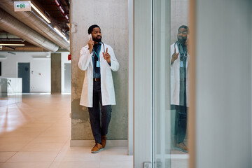 Black doctor talking on cell phone in hallway of hospital.