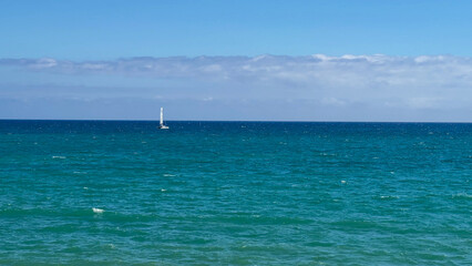 Obraz premium Sailboat on vast ocean horizon under clear blue sky, symbolizing freedom and adventure in serene nautical scene