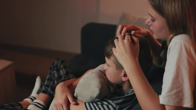 Teenage sister comforting distressed younger brother, softly brushing hair while sibling hugs pillow, sitting on living room couch