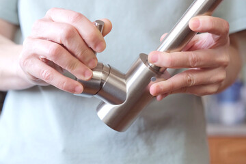 Close-up of hands adjusting a stainless kitchen faucet. Checking the serviceability of a...