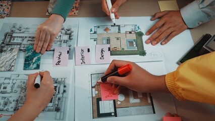A dynamic team collaborates on an interior design project, showcasing hands taking notes, colorful markers, and detailed plans spread across a table, highlighting creative teamwork. SACTR