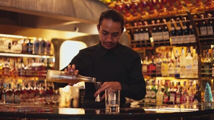 Profile good looking Asian bartender using jigger measure liquor syrup into glass with rock ice at luxurious beverage counter bar scene, neat professional barman costume at nightclub luxury. Vinosity.