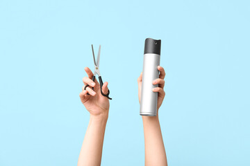 Female hands with scissors and hairspray on color background.