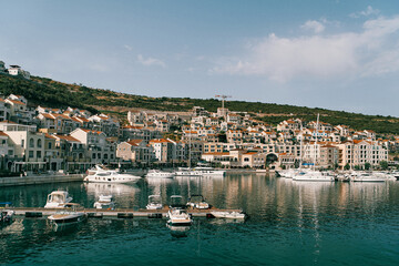 Motor yachts stand along the pier in Lustica Bay against the backdrop of colorful buildings at the foot of the mountains. Montenegro
