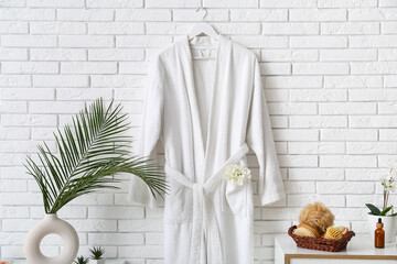 White bathrobe hanging on wall and different bath supplies on chest of drawers in bathroom