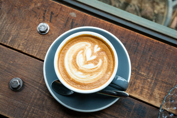 Hot coffee latte with latte art milk foam in cup mug on wood desk on top view. As breakfast In a...