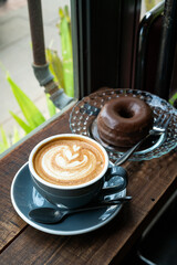 Hot coffee latte with latte art milk foam in cup mug and Homemade chocolate Donut on wood desk on top view. As breakfast In a coffee shop at the cafe,during business work concept,vintage style