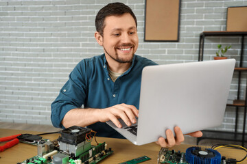 Male technician with laptop repairing computer at table in service center