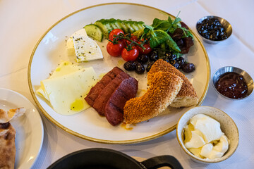 Turkish or Mediterranean style breakfast. Turkish breakfast. Variety of fresh vegetables, olives, cheeses, jams and spreads on a small plates on a white tablecloth covered table. Traditional turkish 