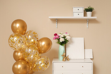 Beautiful golden air balloons with home decor and flowers on commode near beige wall at home