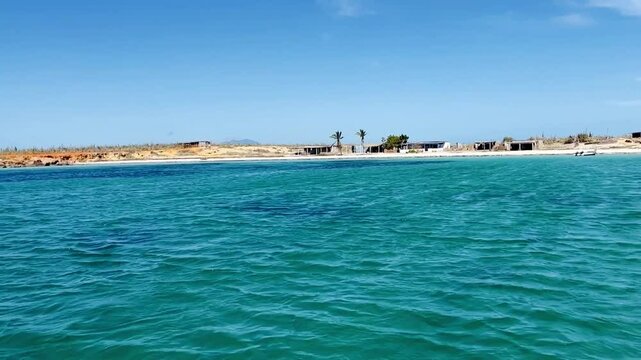 Crystal turquoise waters ripple under the sun as a catamaran glides along the rocky shores between Cubagua and Margarita Island, Venezuela. A tropical paradise with blue skies and vibrant seascapes 4K