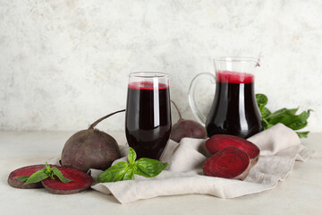 Glass and jug of fresh beet juice with basil on white background