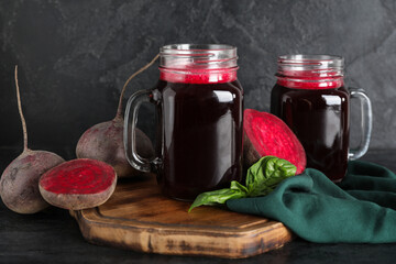 Mason jars of fresh beet juice with basil and vegetables on black background