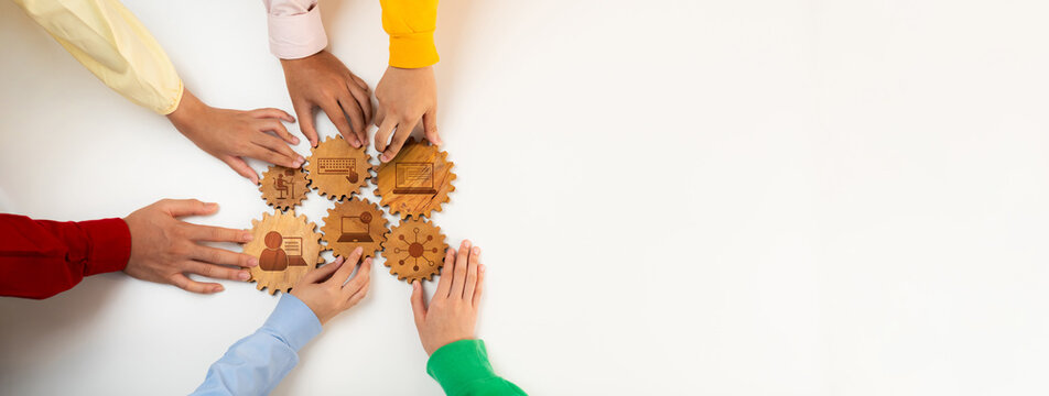 A group of diverse hands works together to assemble wooden gears on a light surface, symbolizing teamwork, synergy, and creative problem solving in a collaborative environment. Amity