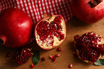 Fresh ripe pomegranates with seeds and leaves on wooden background, closeup