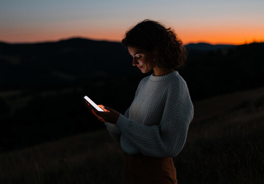 Young woman using smartphone outdoors at sunset, blending technology and nature