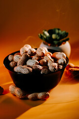 Bowl filled with unpeeled peanuts on a table with a succulent plant in the background during warm lighting