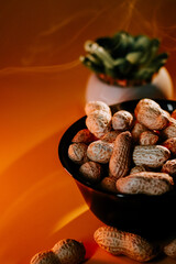 Peanuts in a black bowl on a warm orange background with a decorative plant