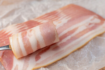 A piece of delicious bacon is carefully being sliced with a fork