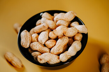 Freshly harvested peanuts in a black bowl on a bright yellow background for a vibrant snack presentation