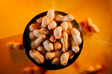 Bowl of roasted peanuts placed on a table with an orange background in a warm setting