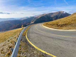 A serpentine road in the mountains features a yellow side line