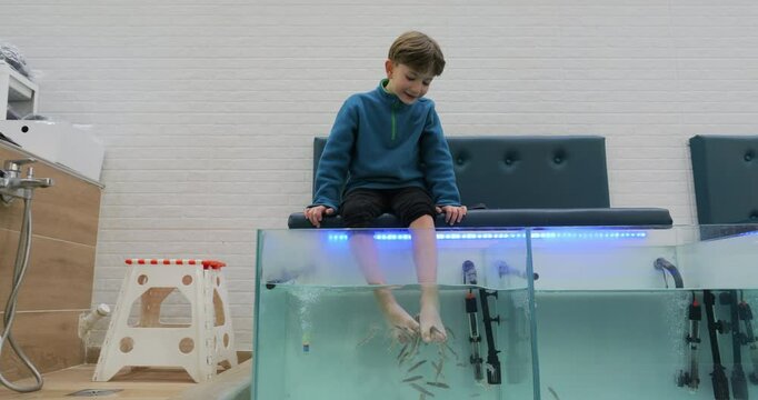 Little boy with his feet into the aquarium with doctor fish
