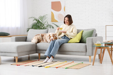 Fototapeta premium Beautiful young woman drinking green tea while sitting with her dog on sofa at home