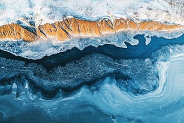 Aerial view of a frozen river flowing beside snow-covered, ochre-colored mountains.
