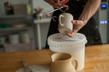 Close-up of a potter's hands glazing a ceramic mug. 