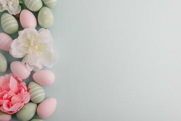 Pastel easter eggs and flowers on green background. Top view