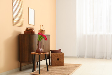 Wooden cabinet with bouquet of beautiful tulip flowers and decor near beige wall
