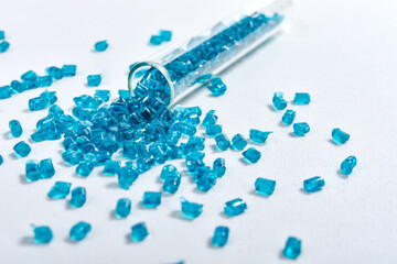 Clear blue masterbatch granules spilled from glass tube and isolated on white background. Color...