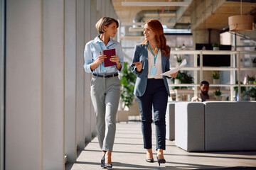 Fototapeta premium Smiling female entrepreneurs communicating while walking through office.