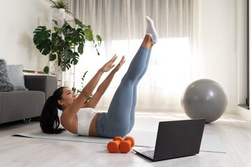 A fit young woman in sportswear performs an abdominal exercise while following an online workout on...