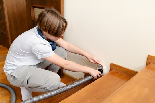 Teenager engages in home cleaning by vacuuming the stairs while managing school assignments and responsibilities. Closeup of plugging central vacuum cleaner hose in to wall inlet socket.