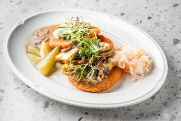 A beautifully plated dish featuring crispy fried fish topped with savory mushroom sauce, garnished with microgreens, and accompanied by pickled vegetables and shrimp on a white oval plate.