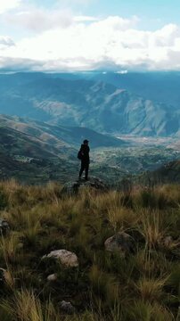 VIDEO VERTICAL Joven viajero con mochila contemplando el paisaje desde la cima de la monta&ntilde;a. Turista explorador en la naturaleza, disfrutando de la libertad y la aventura