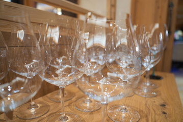 Several clear wine glasses are neatly arranged on a wooden surface, with light reflections and wooden paneling creating a warm, elegant ambiance.
