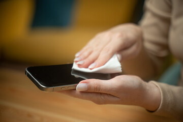 A person is carefully wiping a smartphone screen with a cloth to remove dirt and fingerprints. This activity takes place in a comfortable indoor space during the day.