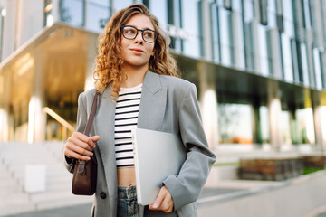 Smiling  woman walking in city street with laptop going to work in the morning. Business, education, freelancer