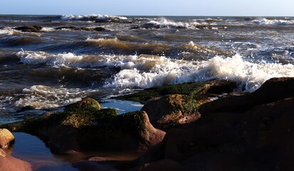 A seascape. A raging ocean. Close-up. Colorful background. Reefs in the foreground. Wallpaper. Poster. Postcard