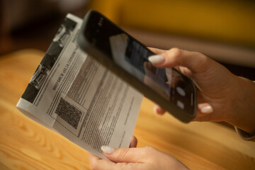 A woman holds her smartphone over a letter, scanning the QR code. The background features soft lighting and a comfortable atmosphere, enhancing her focus on the task.
