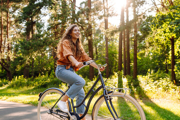 Fototapeta premium Young modern woman rides bicycle in the park. Sports activities. Taking care of environment